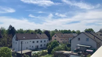 Weitläufiger Blick über eine Wohnsiedlung mit Gärten und Bäumen unter einem hellblauen Himmel.