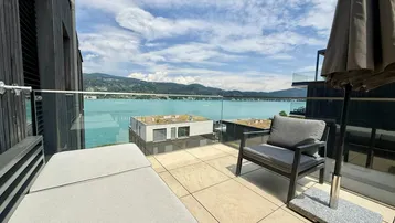 Große Terrasse mit bequemen Lounge-Möbeln und atemberaubendem Blick auf den See und die Berge.