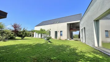 Modernes Haus mit großem Garten und gepflegtem Rasen unter blauem Himmel.