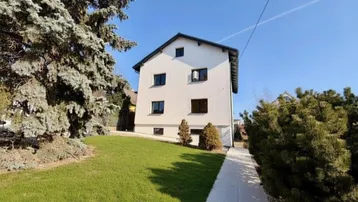 Modernes weißes Einfamilienhaus mit gepflegtem Vorgarten unter blauem Himmel.