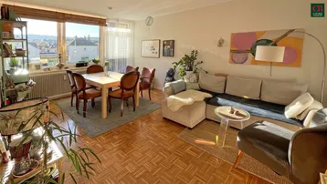 Helles Wohn- und Esszimmer mit Parkettboden, großen Fenstern und einem weiten Blick über die Stadt.