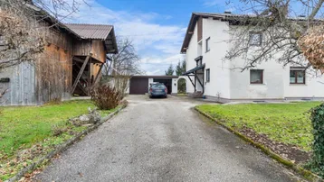 Zufahrt zu einem Wohnhaus und einer Scheune mit einem Auto auf dem Kiesweg.