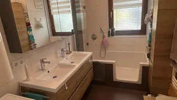Modernes Badezimmer mit Doppelwaschbecken, Badewanne mit Dusche und Waschmaschine.