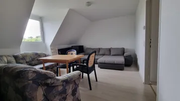 Gemütliches Wohnzimmer im Dachgeschoss mit schrägen Wänden, Laminatboden und Blick ins Grüne.