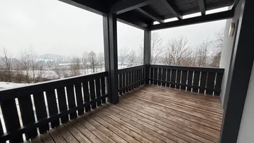 Überdachter Balkon mit Holzboden und Blick auf die verschneite Landschaft und Berge.