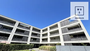 Moderne Wohnanlage mit Holzfassade und zahlreichen Balkonen unter blauem Himmel.
