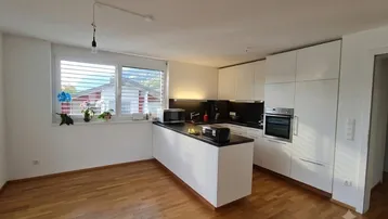 Helle, moderne Küche mit weißer Kücheninsel, Einbaugeräten und Holzfußboden.