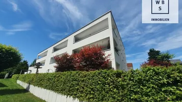 Modernes Mehrfamilienhaus mit klaren Linien und gepflegter Hecke unter blauem Himmel.