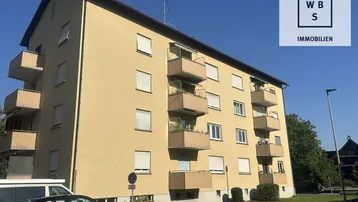 Mehrfamilienhaus mit gelber Fassade und mehreren Balkonen unter blauem Himmel.