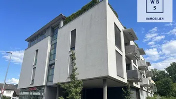 Modernes Mehrfamilienhaus mit klarer Architektur, Balkonen und begrüntem Flachdach unter blauem Himmel.