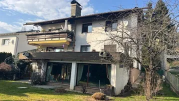 Großzügiges Einfamilienhaus mit Balkonen, großen Fenstern und einem gepflegten Gartenbereich.