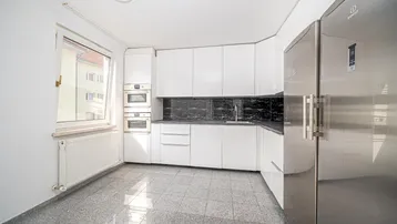 Moderne Küche mit weißen Hochglanzschränken, dunkler Arbeitsplatte und integrierten Geräten.