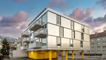 Modernes Wohngebäude mit Balkonen, großen Fenstern und auffälligen gelben Stützen im Erdgeschoss.