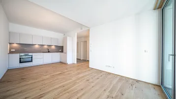 Moderne Einbauküche in hellem Raum mit Holzboden, offen zum Wohnbereich.