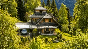 Charmantes Holzhaus in alpiner Umgebung, umgeben von üppigem Grün und hohen Bäumen.