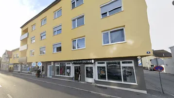 Mehrstöckiges Gebäude mit gelber Fassade, Rollläden an den Fenstern und Balkonen an der Seite.