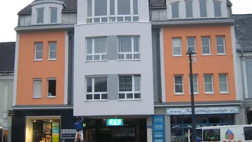 Modernes Mehrfamilienhaus mit gemischter Nutzung, orangefarbener und grauer Fassade sowie großen Fenstern.
