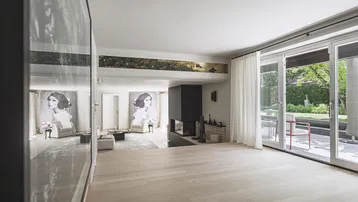 Helles Wohnzimmer mit Holzboden, großzügigen Fensterfronten und Blick auf den Garten und Poolbereich.