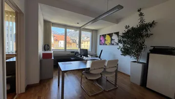 Heller Büroraum mit Holzboden, großen Fenstern und Bergblick, ideal für eine angenehme Arbeitsatmosphäre.