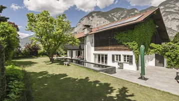 Malerisches Anwesen mit großem Garten, Pool und beeindruckendem Bergblick unter blauem Himmel.