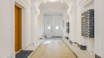 Heller Eingangsbereich mit kunstvollen Stuckverzierungen, historischen Fliesen und Briefkästen.