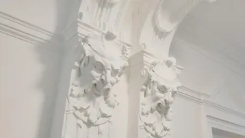 Detailaufnahme einer prunkvollen Stuckdecke und verzierten Säulen im historischen Eingangsbereich.