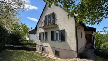 Klassisches Einfamilienhaus mit Balkon, Fensterläden und gepflegtem Vorgarten unter blauem Himmel.