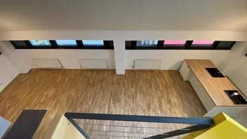 Offener Wohnbereich mit Holzboden, moderner Kücheninsel und vielen Dachfenstern, von oben gesehen.