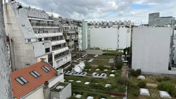 Blick über begrünte Dächer und umliegende Gebäude in einer städtischen Umgebung unter bewölktem Himmel.