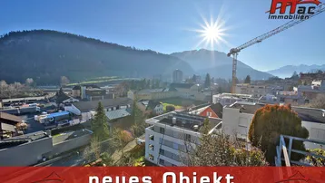 Panoramablick über die Stadt mit Bergen im Hintergrund und strahlendem Sonnenschein.