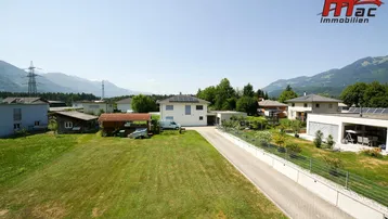 Weitläufige Ansicht von Wohnhäusern in ländlicher Umgebung mit grünen Feldern und Bergen.