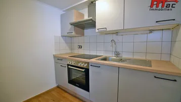 Kleine, funktionale Küchenzeile mit hellgrauen Schränken, Kochfeld und Backofen.