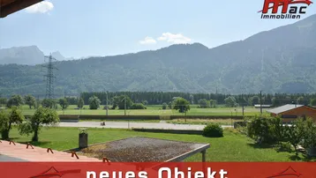 Weitläufiger Blick auf die umliegende Berglandschaft und grüne Felder unter blauem Himmel.