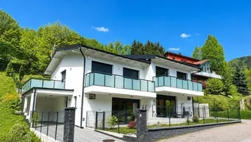 Moderne weiße Doppelhaushälfte mit Balkonen, Carport und gepflegtem Vorgarten in grüner Umgebung.