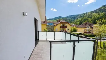 Geräumiger Balkon mit Fliesenboden und Glasgeländer, bietet Blick auf die umliegende Landschaft.