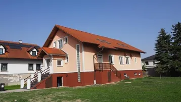 Haus mit orangefarbener Fassade und rotem Ziegeldach auf einem grünen Grundstück.