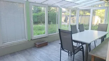 Heller Essbereich im Wintergarten mit großen Fenstern und Blick ins Grüne.
