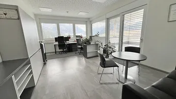 Geräumiges und helles Büro mit mehreren Arbeitsplätzen, modernen Möbeln und großen Fenstern mit Bergblick.