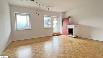 Helles Wohnzimmer mit Parkettboden, Kachelofen und Zugang zur Terrasse mit Bergblick.