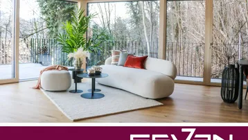 Helles, modernes Wohnzimmer mit großen Fenstern, Holzboden und Blick ins Grüne.