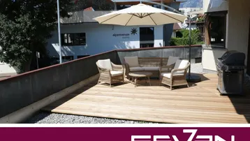 Geräumige Terrasse mit Holzboden, Gartenmöbeln, Sonnenschirm und Grill, ideal für entspannte Stunden im Freien.