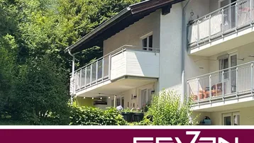 Mehrfamilienhaus mit mehreren Balkonen, umgeben von üppigem Grün und Bäumen.