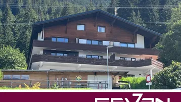 Traditionelles Holzhaus in den Bergen mit mehreren Balkonen und umgeben von Nadelbäumen.