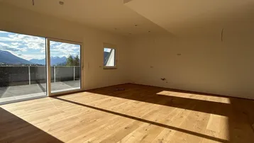 Helles, leeres Zimmer mit Holzboden und Zugang zu einem Balkon mit Bergblick.