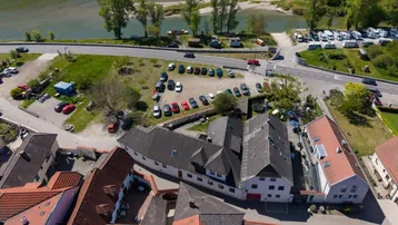 Luftaufnahme eines Dorfes am Flussufer mit umliegenden Gebäuden, Parkplätzen und grüner Landschaft.