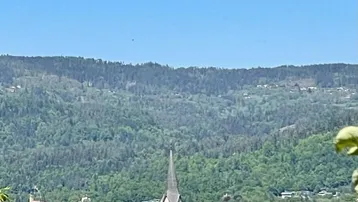 Idyllischer Blick auf eine Kirche auf einer Insel im See, umgeben von bewaldeten Hügeln unter blauem Himmel.