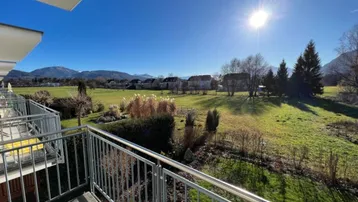 Sonniger Balkon mit Blick auf grüne Wiesen und die umliegende Berglandschaft.