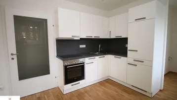 Moderne Einbauküche mit weißen Schränken, dunkler Arbeitsplatte und integriertem Backofen.