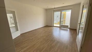 Heller Wohnraum mit Laminatboden und Zugang zu einem französischen Balkon.