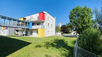 Modernes Gebäude mit farbigen Akzenten und gepflegter Grünfläche unter blauem Himmel.